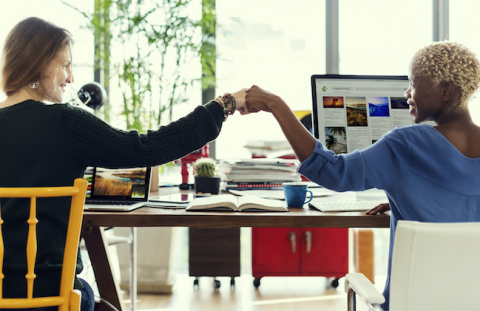 Two women fist bump at adjacent desks