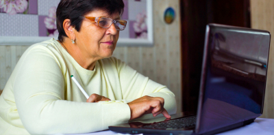 An older woman sitting at a kitchen table and using a laptop