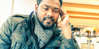 A south Asian man in leather jacket looking at his laptop in a cafe