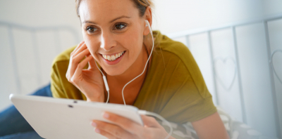 A woman using her tablet with a pair of white headphones, looking excited