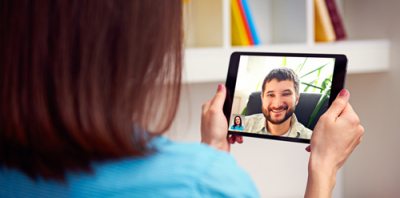 A woman holding a tablet computer. On the tablet is an image of a smiling man she is having a video call with.