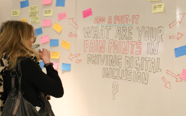 woman looking at  whiteboard that says "what are your pain points driving digital inclusion?"