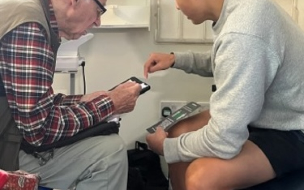 an older and younger person at a digital drop in looking at a tablet