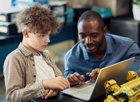 young person being helped at a computer by an older person