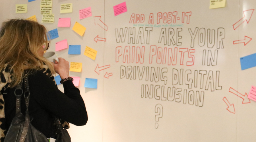 woman looking at  whiteboard that says "what are your pain points driving digital inclusion?"